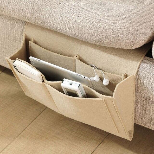 Beige BedCaddy hangend aan zijkant van een beige bank met een iPad en telefoon erin.