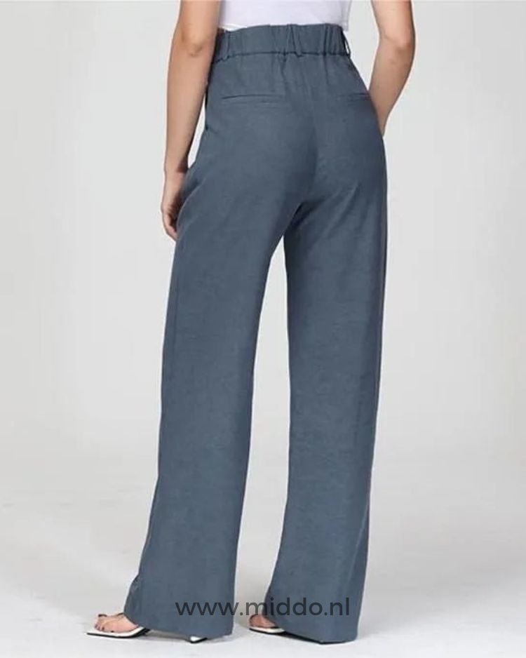 Een vrouw heeft de wijde blauwe pantalon aan maar laat nu de pantalon zien met 2 zakken op de achterkant van de broek.