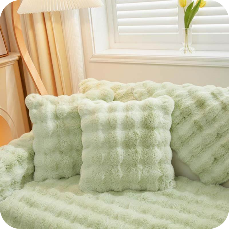 Groene pluche kussens en deken op een bank bij een raam